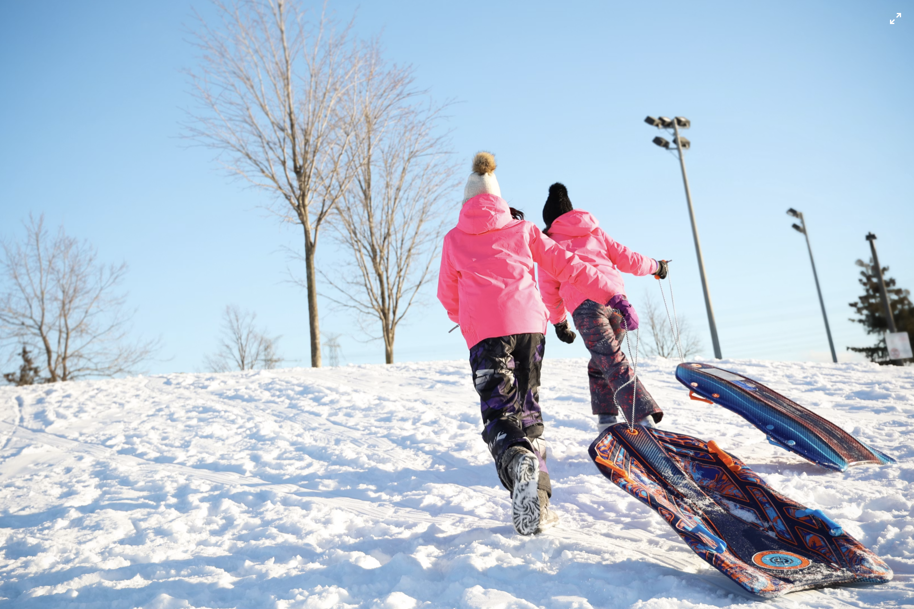 two kids running up a snowhill with sleds